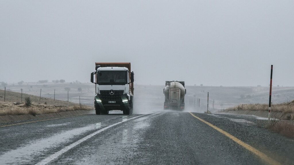 Dois camiões a circular numa autoestrada com chuva e céu encoberto